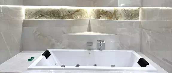 An illuminated bathtub in front of a curved wall with niches and light-grey, large tiles
