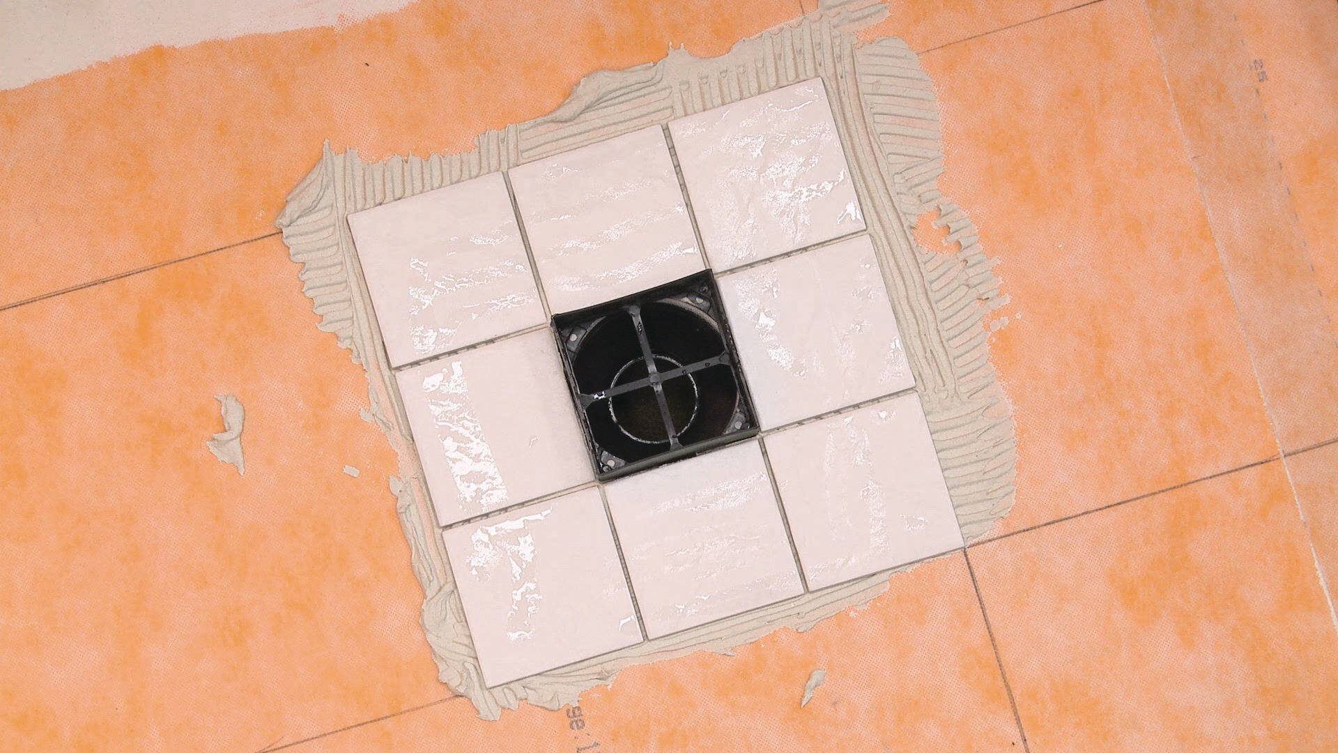 Un sol de douche non fini, montrant une membrane orange et des carreaux installés proprement autour d'une ouverture de drain.