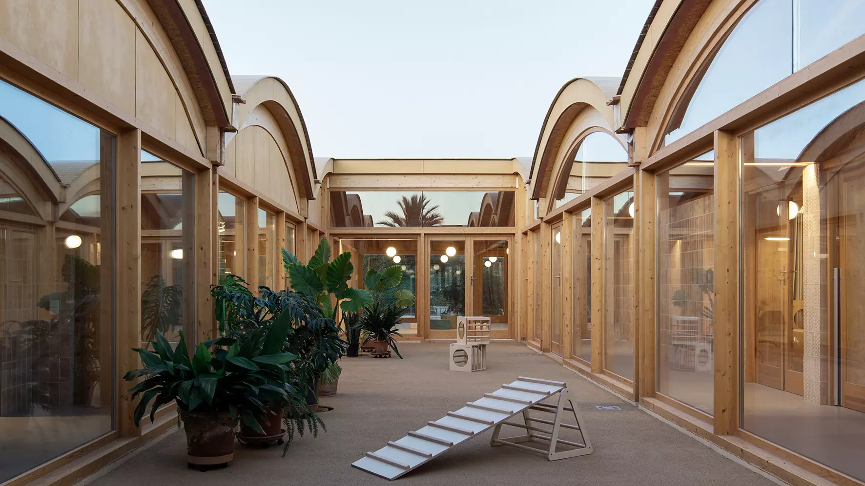 Patio interior de la escoleta infantil de Muro, en Mallorca, con juegos infantiles de madera y plantas grandes
