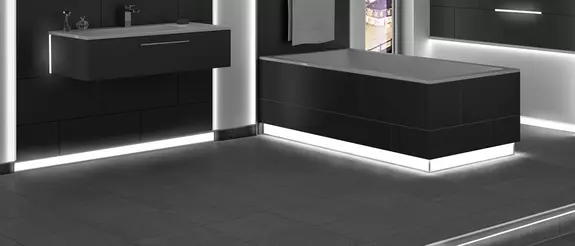 Vloer van een zwart betegelde badkamer met verlichte plintprofielen aan de wand en de rand van het bad