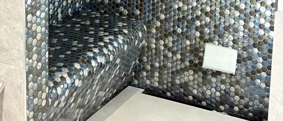Bench tiled with greay, white and blue hexagon tiles in a shower