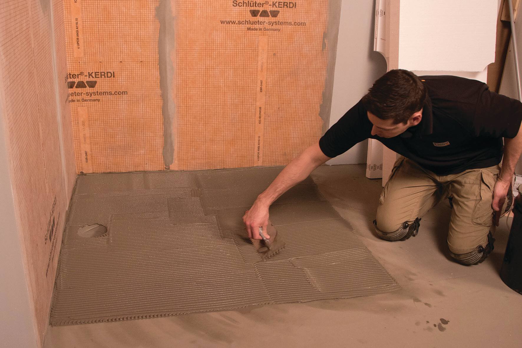 Un installateur applique le mortier-colle Schluter sur le substrat de la douche à l'aide d'une truelle.