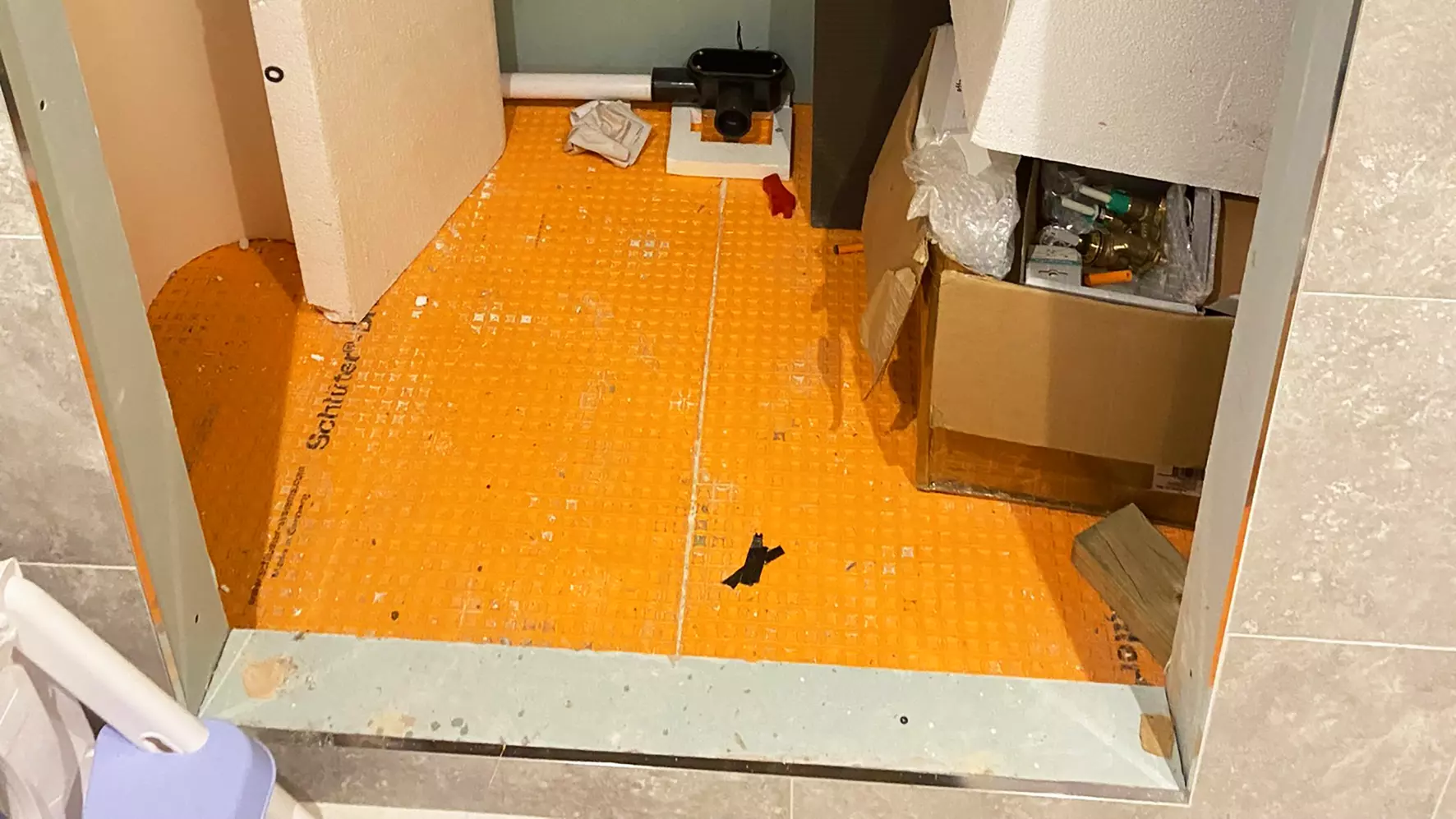Shower entrance with light grey tiles and orange Schl&uuml;ter-DITRA mat on the shower floor