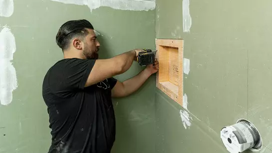 Řemesln&iacute;k přišroubov&aacute;v&aacute; niku z oranžov&yacute;ch desek KERDI-BOARD do tyrkysov&eacute; s&aacute;drokartonov&eacute; stěny