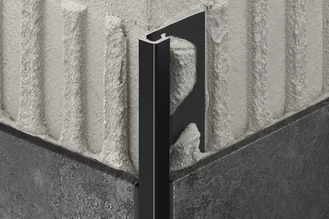 Vue d&eacute;taill&eacute;e du profil&eacute; Schl&uuml;ter-QUADEC-AC avec finition TRENDLINE MGS, noir graphite mat, sur un angle sortant de mur avec carrelage de couleur anthracite