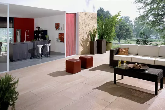 Een huis met aangrenzende tuin en een terras met een zitbank en open bar.