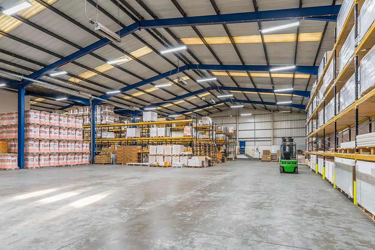 A wide angle shot of Schl&uuml;ter's warehouse in the UK. Shelving full of product is in the far left corner and along the right hand side. A parked green forklift truck is next to the shelving