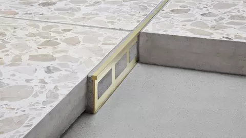 Vista detallada del perfil de separaci&oacute;n y decorativo Schl&uuml;ter-TERRAZZO-M en dorado.