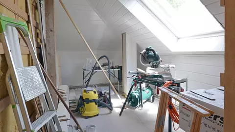 Aanzicht van de vroegere werkkamer met schuin plafond, groot raam en muren in licht hout.