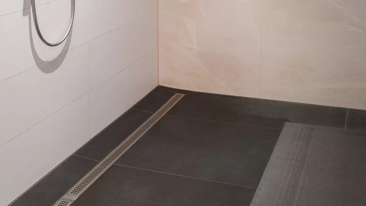 Die fertig gefliesten Duschen im Vereinsheim mit KERDI-LINE Duschrinne, dunkelgrauen Boden- und wei&szlig;en Wandfliesen