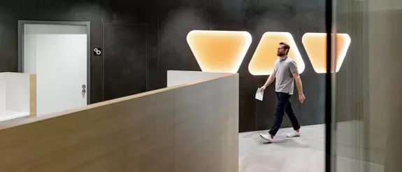 Mitarbeiter l&auml;uft &uuml;ber den Flur, Schl&uuml;ter-Trapeze im Hintergrund an der Wand