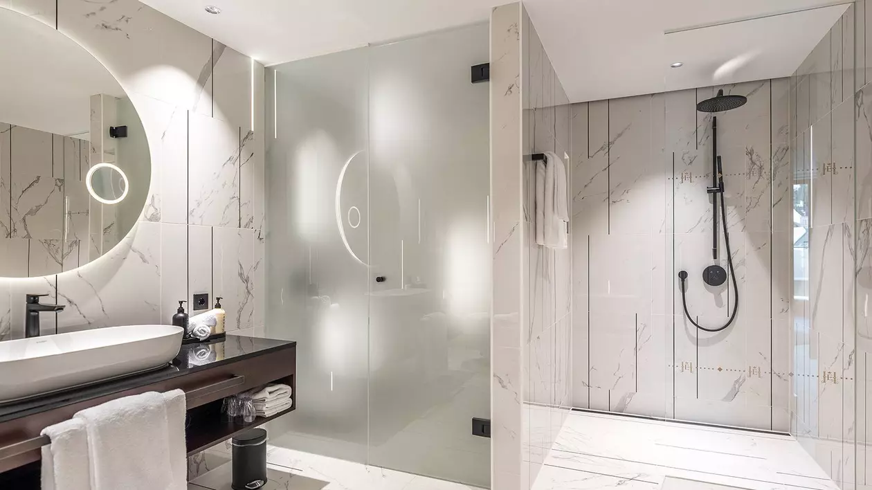 Cuarto de ba&ntilde;o moderno con baldosas de m&aacute;rmol blanco, tecnolog&iacute;a de iluminaci&oacute;n y ducha a ras de suelo