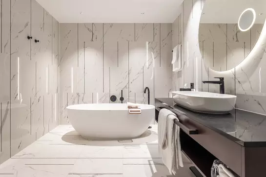Badezimmer mit freistehender Wanne, wei&szlig;en Marmorfliesen an der Wand und beleuchteten Lichtlinien in den Fugen
