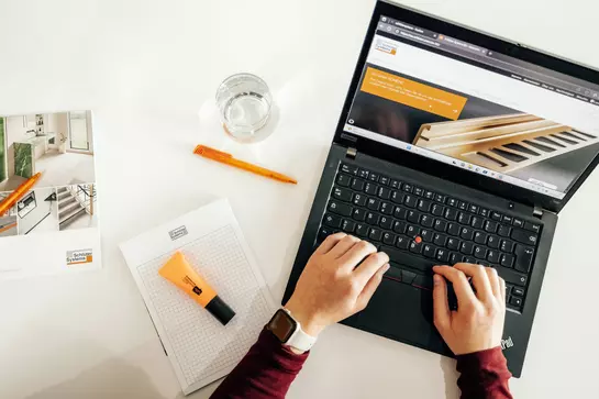 Person arbeitet am Laptop an einem Schreibtisch, daneben liegen Notizblock, Kugelschreiber, Textmarker und Schl&uuml;ter-Systems-Brosch&uuml;re 