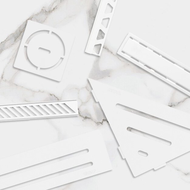 Une présentation de grilles de drain, étagères et profils blancs brillants assortis sur un carrelage en marbre blanc.