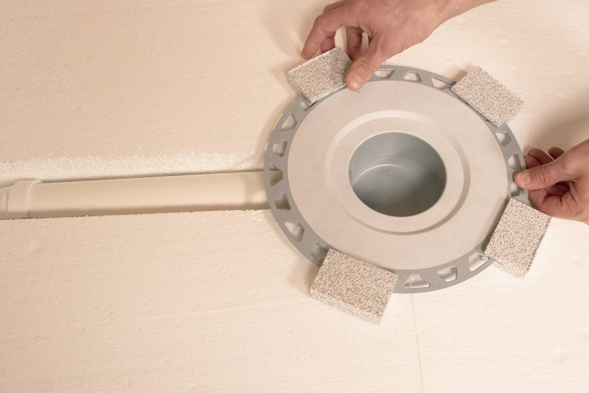 Une bride de drain KERDI-DRAIN-H est fixée au tuyau et à la plaque de compensation.