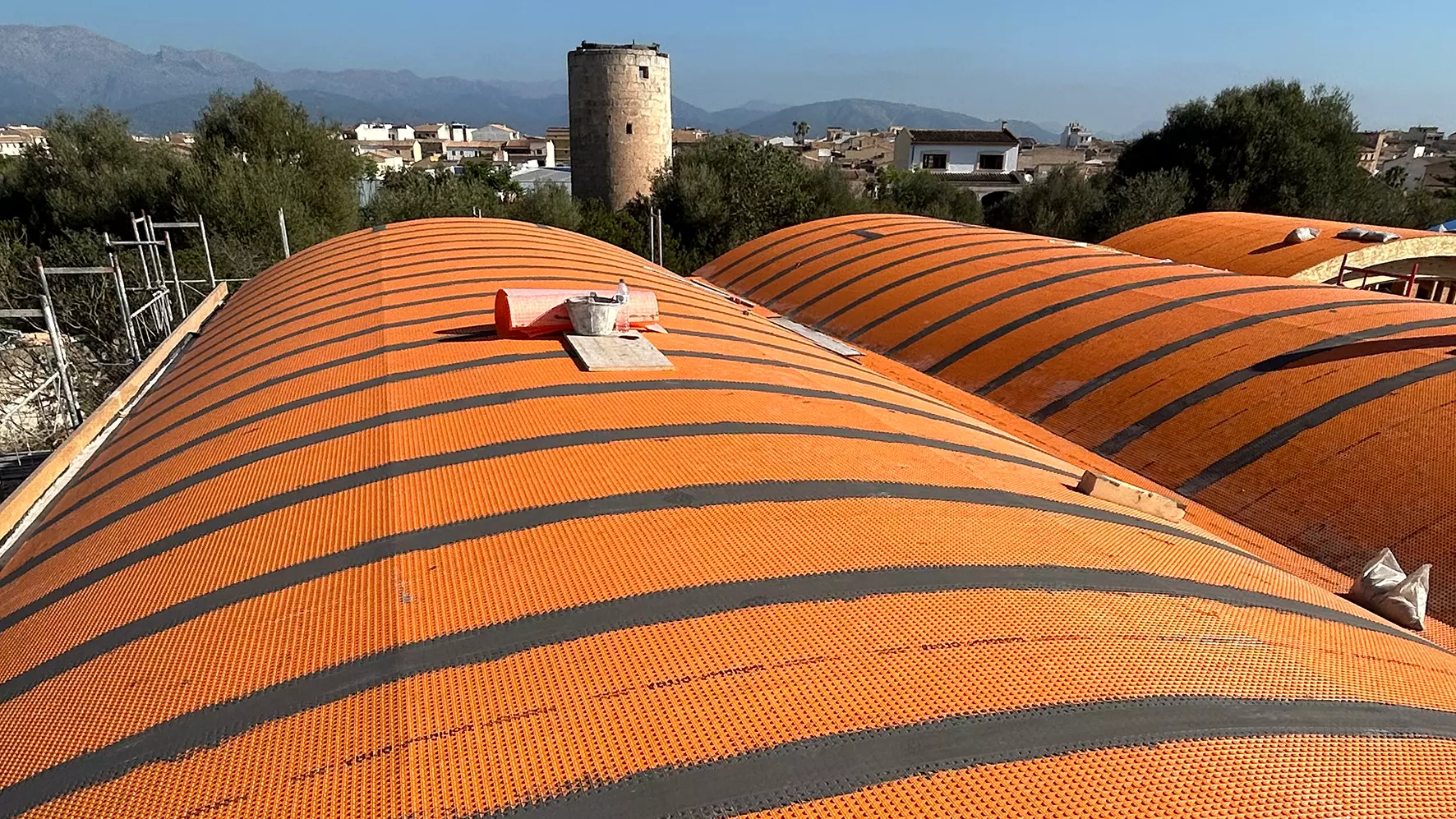 Dos trabajadores colocan la malla de desacoplamiento naranja DITRA sobre los tejados curvos de la escoleta Muro