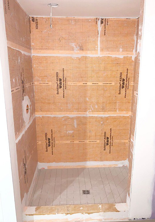 Une douche en construction avec divers produits d'étanchéité de Schluter Systems.