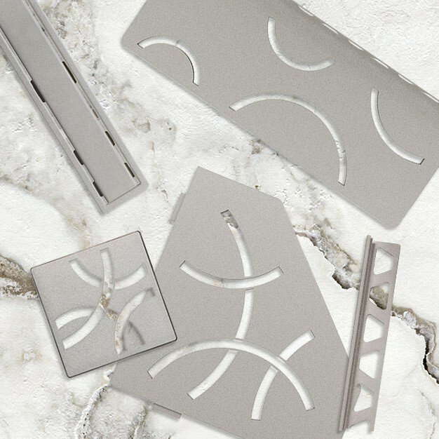 Accessoires de douche gris pierre avec une grille perforée incurvée présentée sur une surface en marbre.