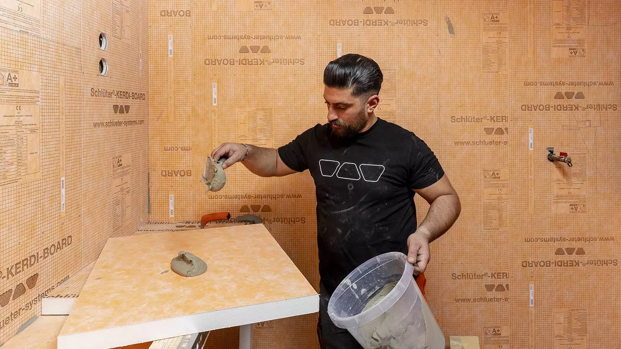 Ein Handwerker verteilt M&ouml;rtel auf orangenen KERDI-BOARD Verlegeplatten