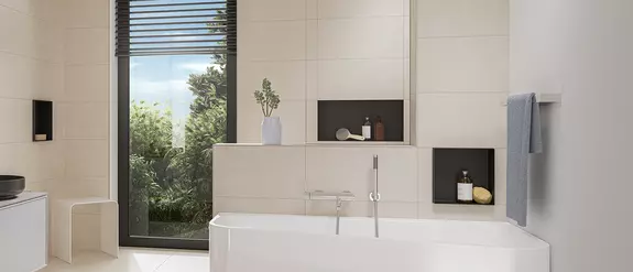Bathroom tiled in light beige with white bathtub and black Schl&uuml;ter-DESIGN-NICHE wall niches