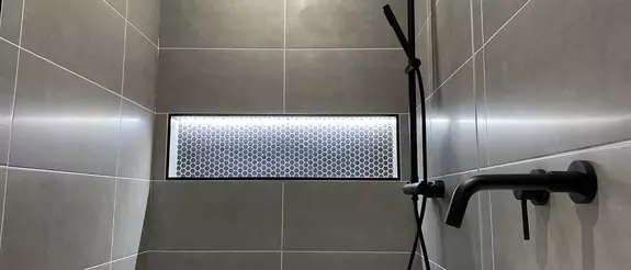Cuarto de ba&ntilde;o en color gris con toques en negro y la hornacina iluminada Schl&uuml;ter-KERDI-BOARD-NLT.