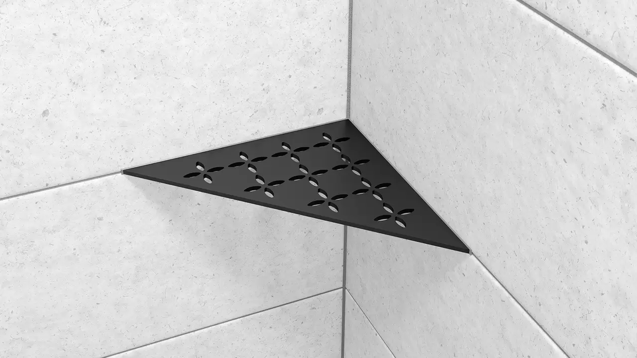 Primer plano del estante de esquina para duchas Schl&uuml;ter-SHELF-E-S1 en forma de tri&aacute;ngulo is&oacute;sceles en dise&ntilde;o FLORAL negro mate MGS, instalado en la pared con cer&aacute;mica gris claro.