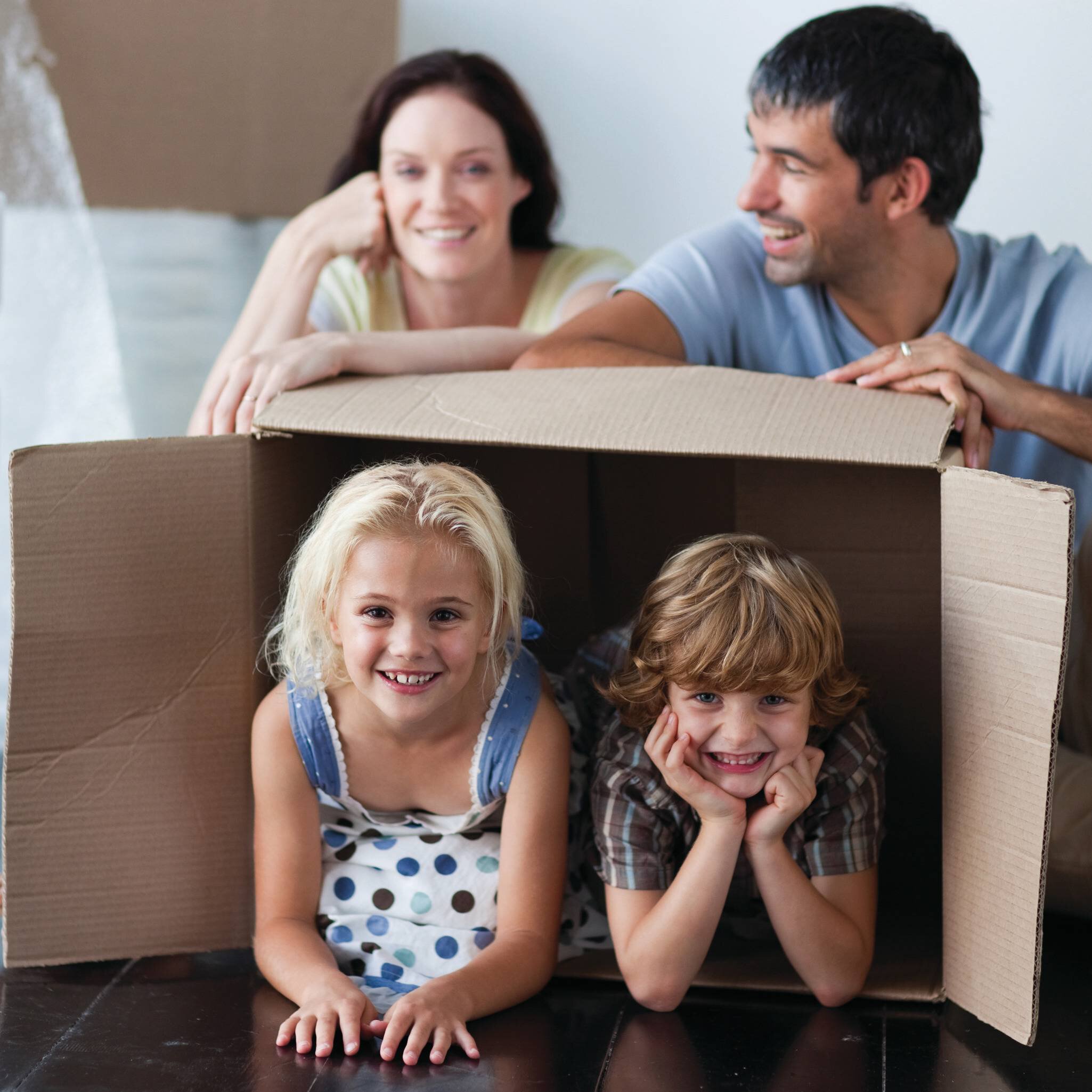 Une famille de quatre personnes joue &agrave; la maison avec un grand carton de d&eacute;m&eacute;nagement dans lequel les enfants se sont gliss&eacute;s