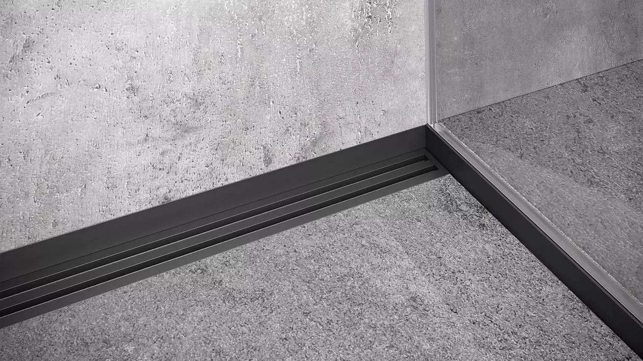 Grau geflieste R&uuml;ckwand einer Dusche mit schwarzer Duschrinne und zus&auml;tzlichen Duschprofilen