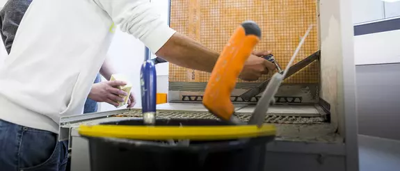 Twee personen bepleisteren in een Schl&uuml;ter-WorkBox-scholing een voorbeeldmodel.