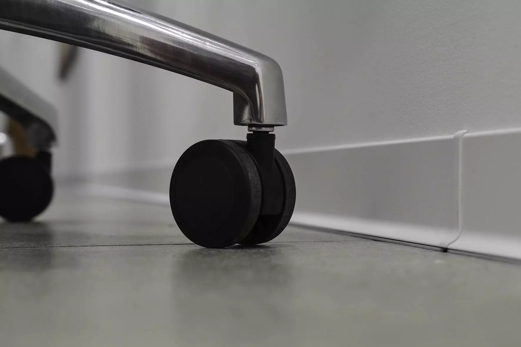 Close-up van de zwarte wielen van een bureaustoel voor een witte plint aan een witte wand