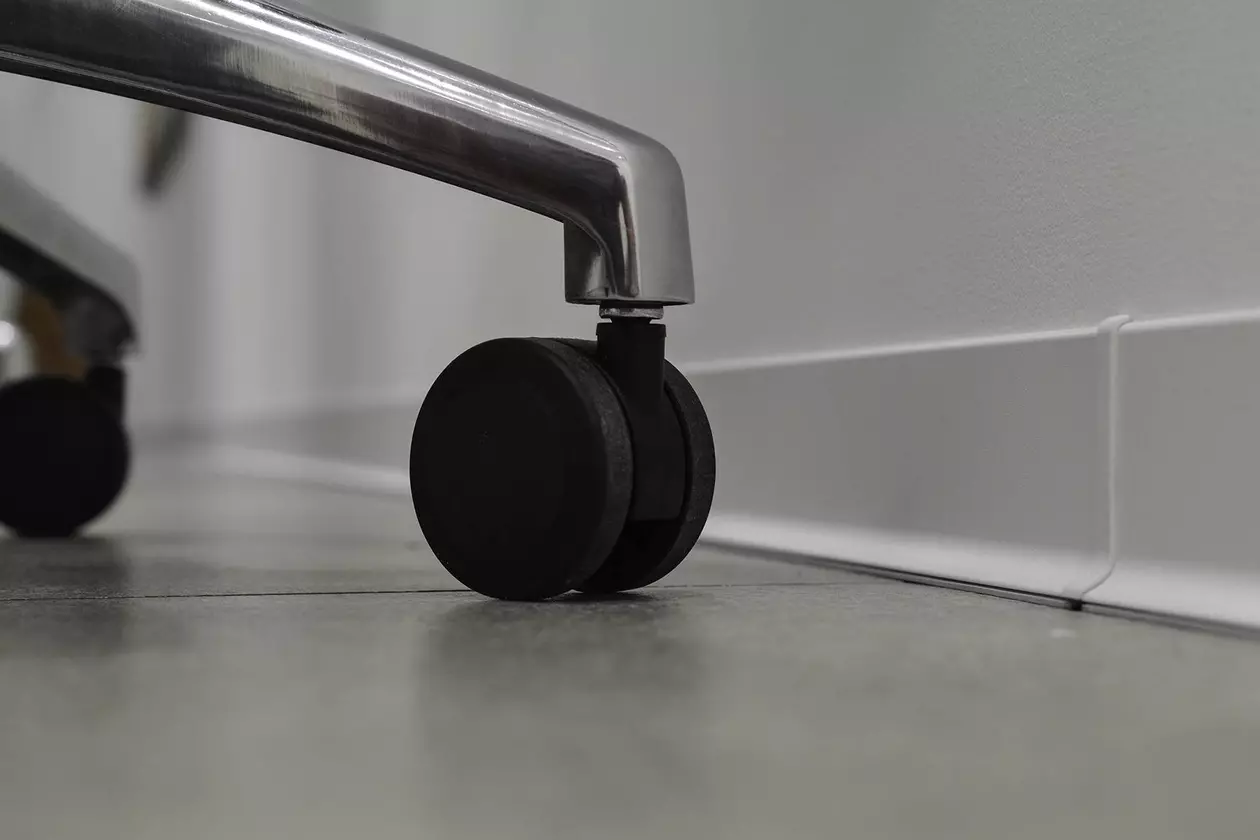 Gros plan sur les roulettes noires d'une chaise de bureau devant une plinthe blanche sur un mur blanc