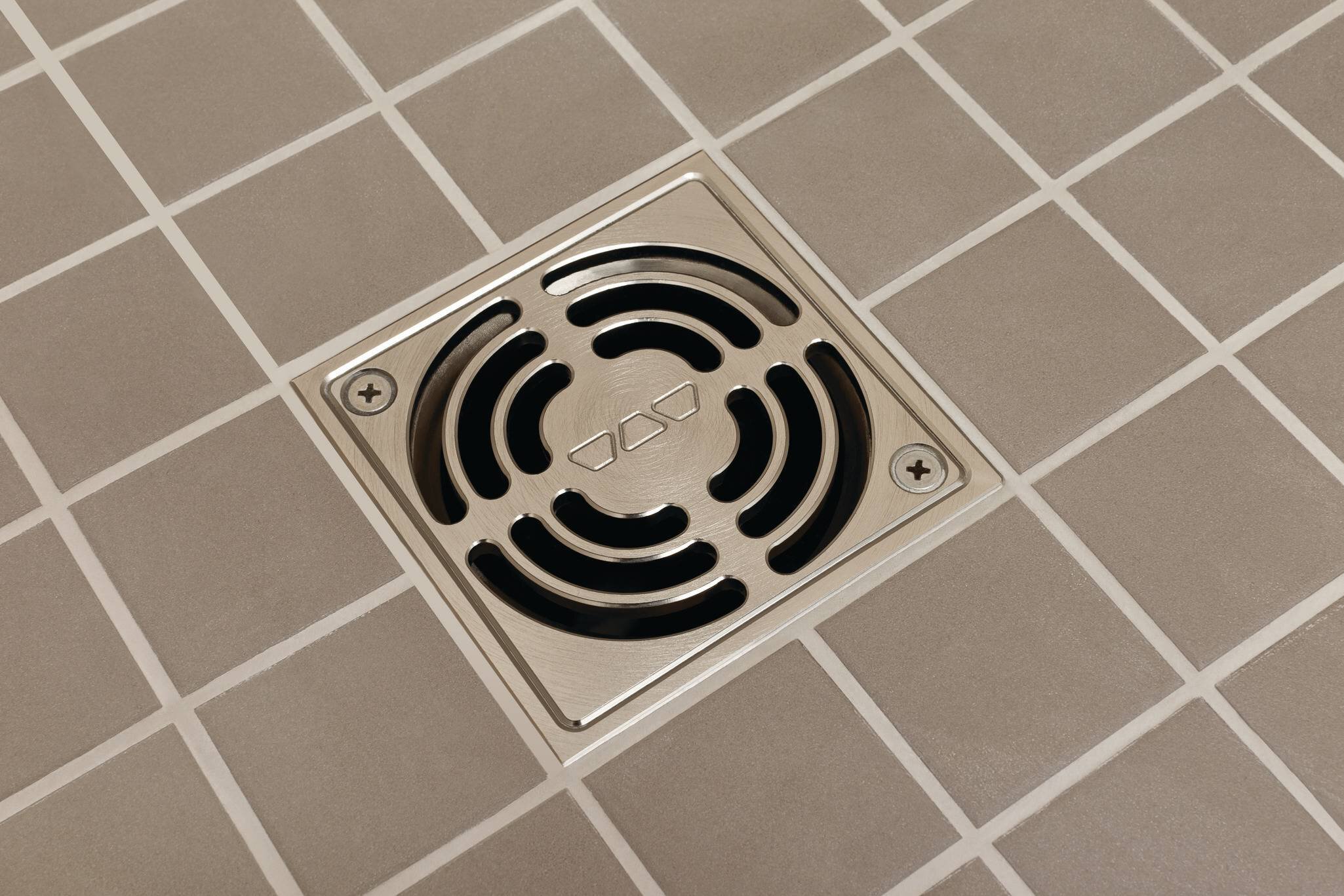 Une vue rapprochée d'un drain de douche avec une grille métallique encastrée dans le sol carrelé, mettant en valeur son design fonctionnel.