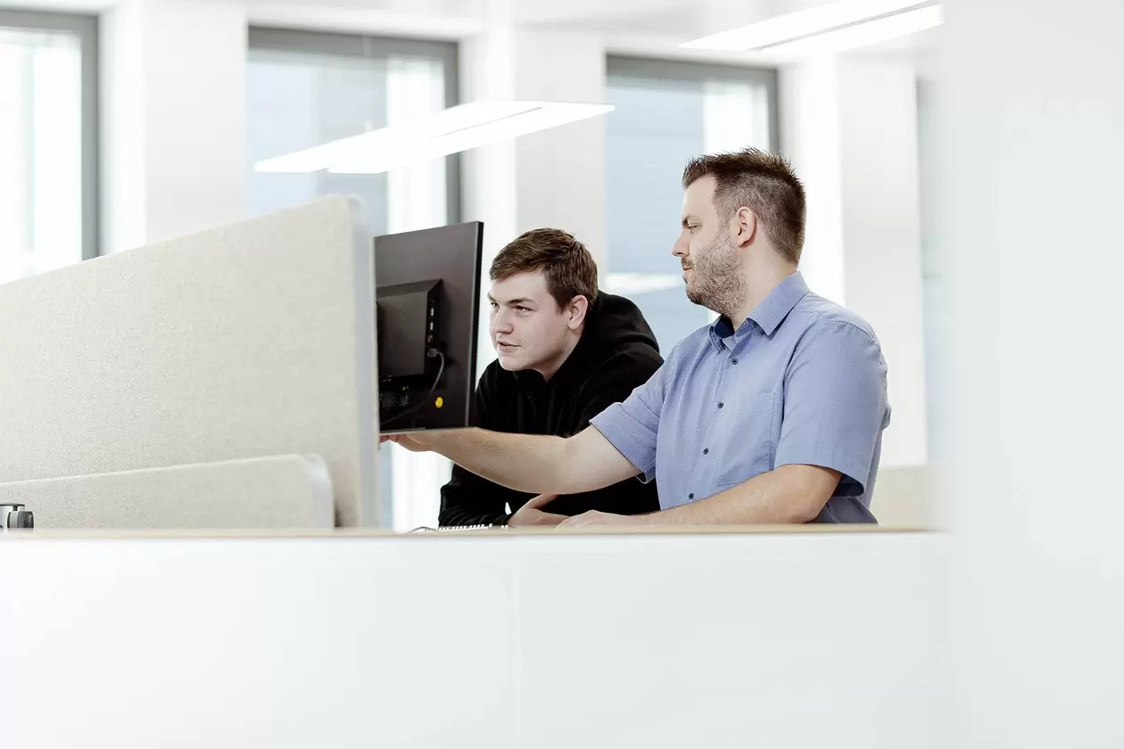 Ausbilder und Azubi blicken gemeinsam auf Computer-Bildschirm