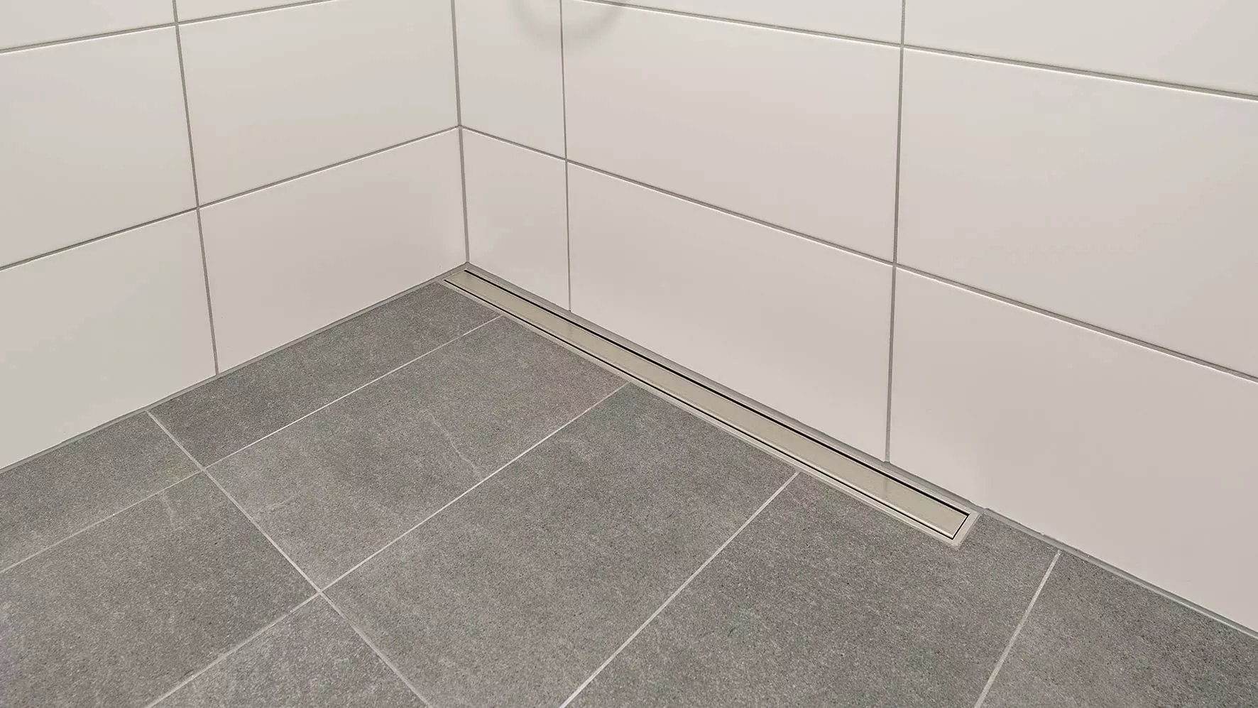 Grau gefliester Boden einer barrierefreien Dusche mit Entw&auml;sserungsrinne aus Edelstahl an der R&uuml;ckwand