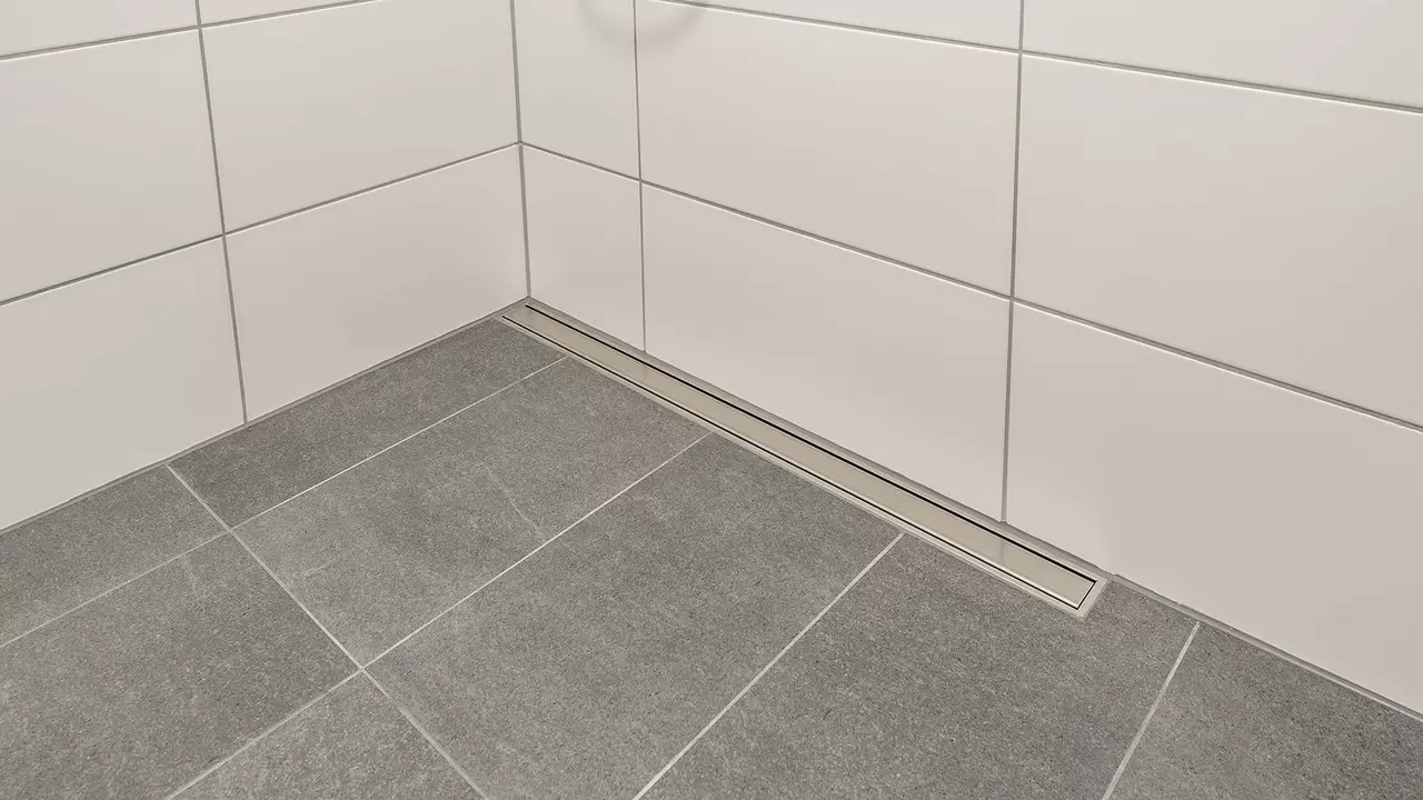 Grau gefliester Boden einer barrierefreien Dusche mit Entw&auml;sserungsrinne aus Edelstahl an der R&uuml;ckwand