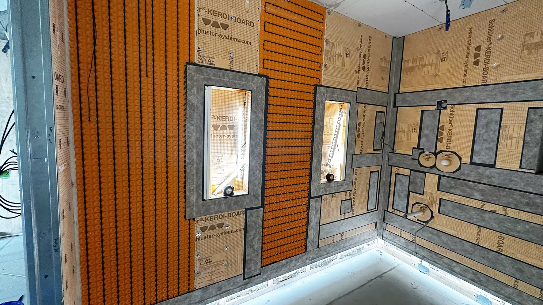 Bathroom construction site with LED-lit wall niches, orange uncoupling mat and heating cables