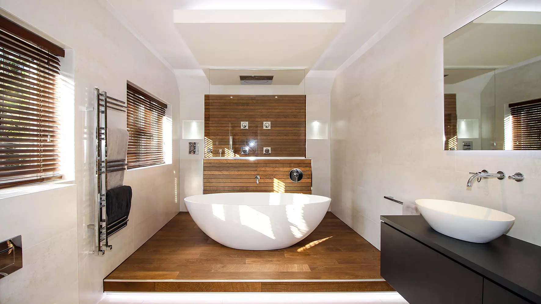 Ba&ntilde;era exenta rodeada de baldosas efecto madera y zona de ducha al fondo.