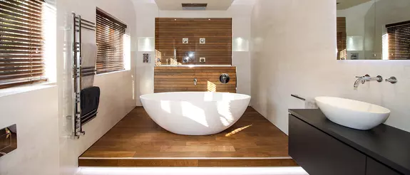 Ba&ntilde;era exenta rodeada de baldosas efecto madera y zona de ducha al fondo.