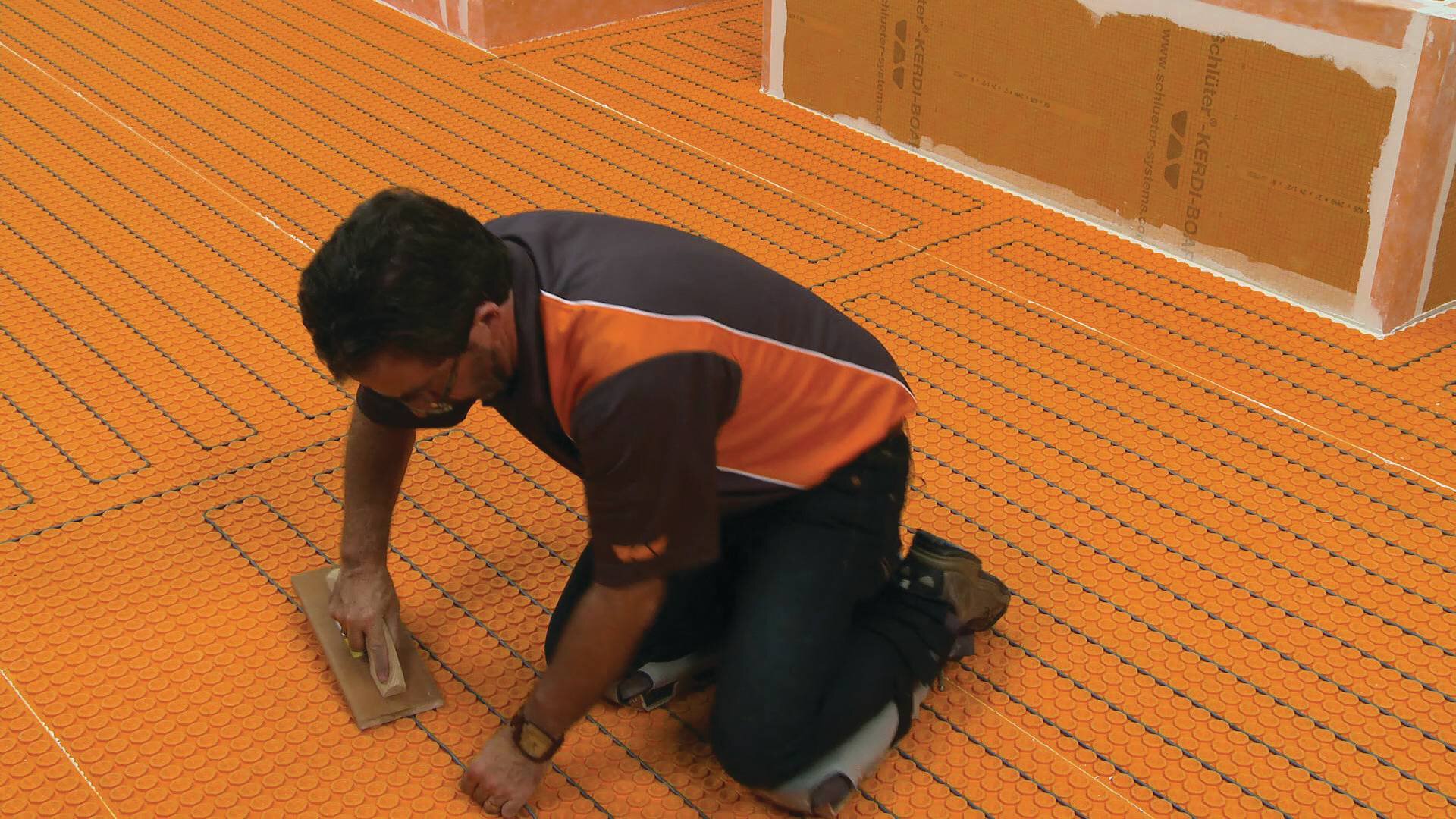 Un homme installe la membrane orange Ditra-Heat sur le sol d'une salle de bains