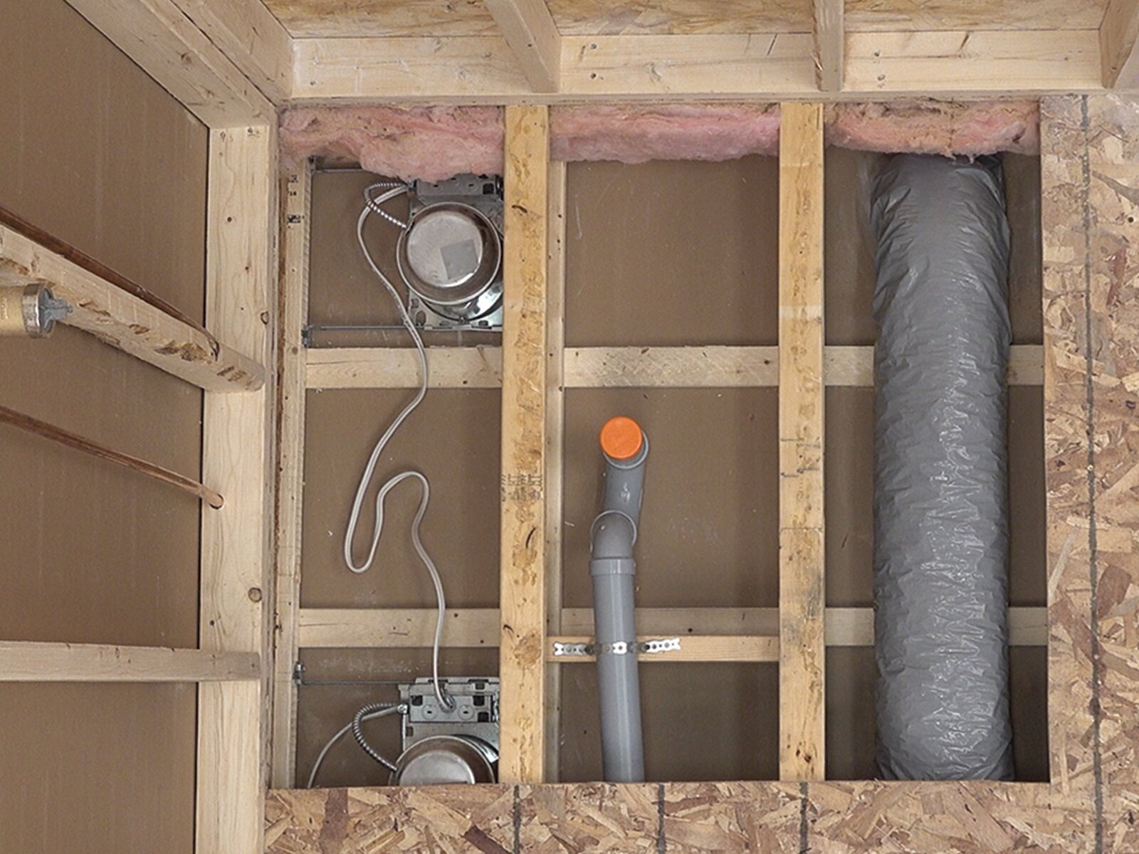 Opened subfloor showing existing plumbing, HVAC, and electrical between joists before a curbless shower remodel
