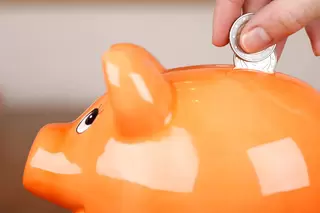 Orangefarbenes Sparschwein wird mit Geld gef&uuml;llt