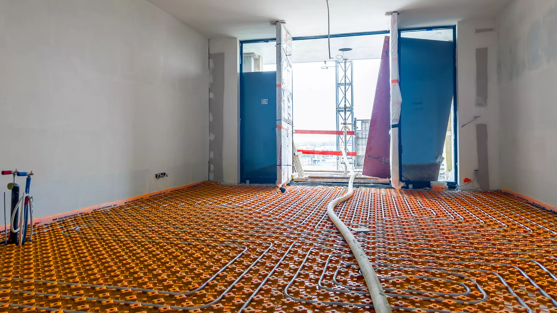Raum der City Dox mit bodentiefen Fenstern im Rohbau mit verlegter BEKOTEC-THERM Matte und Heizrohren