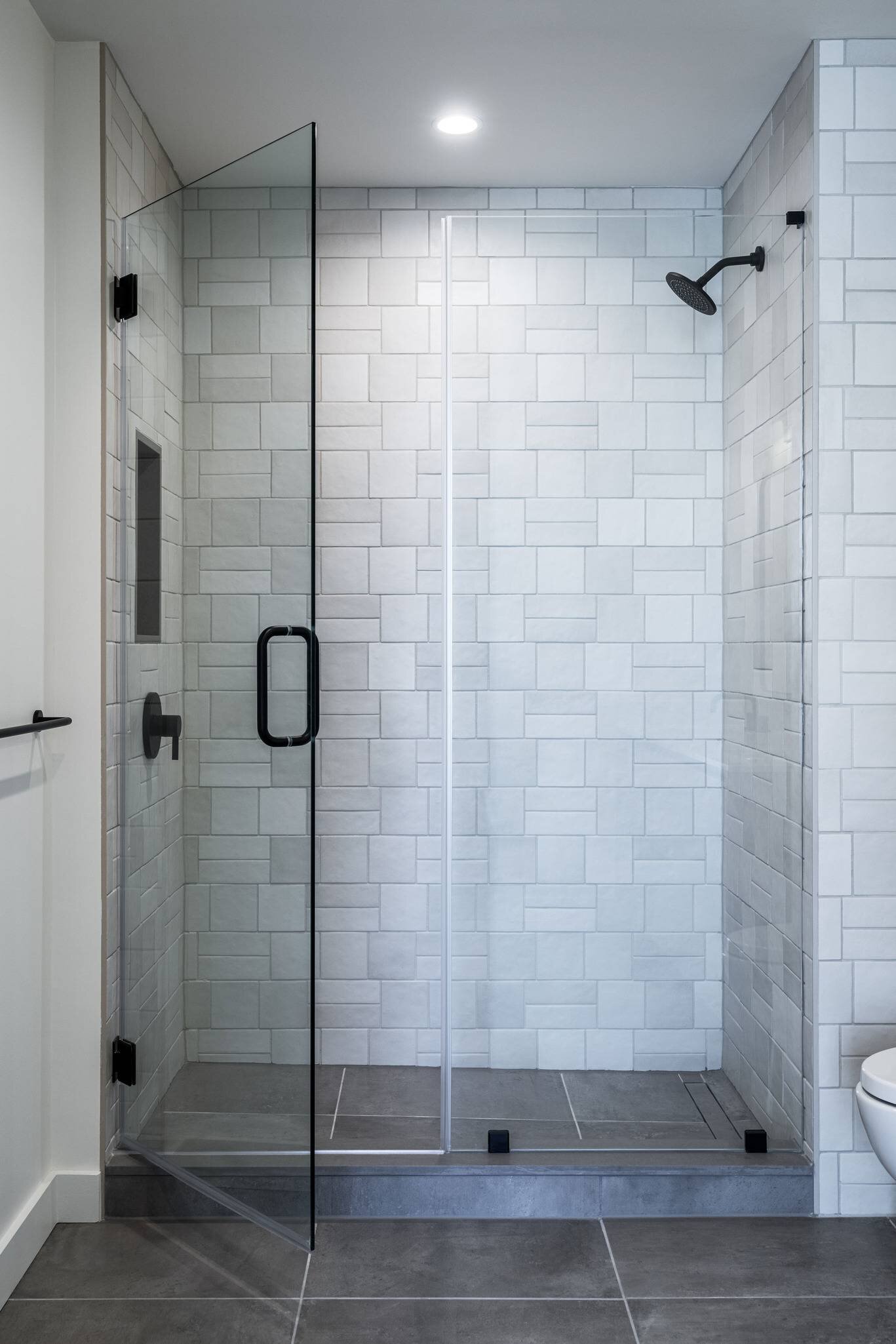 Une douche moderne carrelée avec porte en verre et quincaillerie noire.