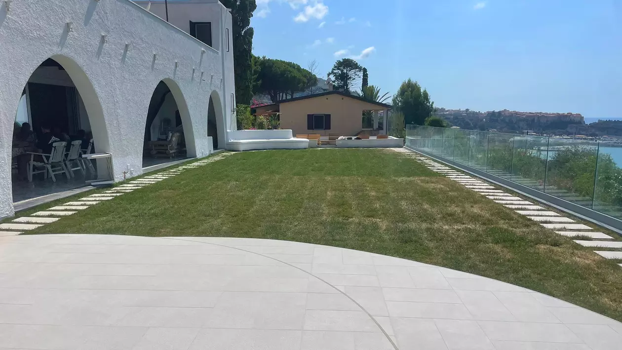 Terrazza sul tetto con prato e balaustra in vetro di fronte a un panorama costiero con vista sul mare 