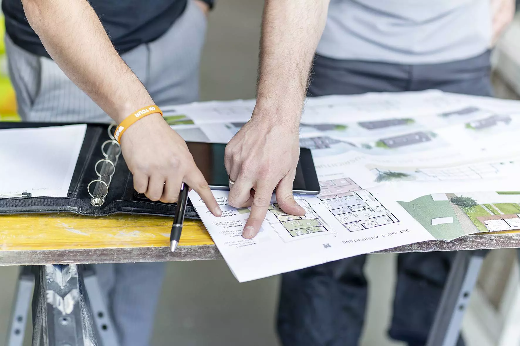 Twee personen wijzen met wijsvingers op een planningsblad over bouwobjecten en overleggen.