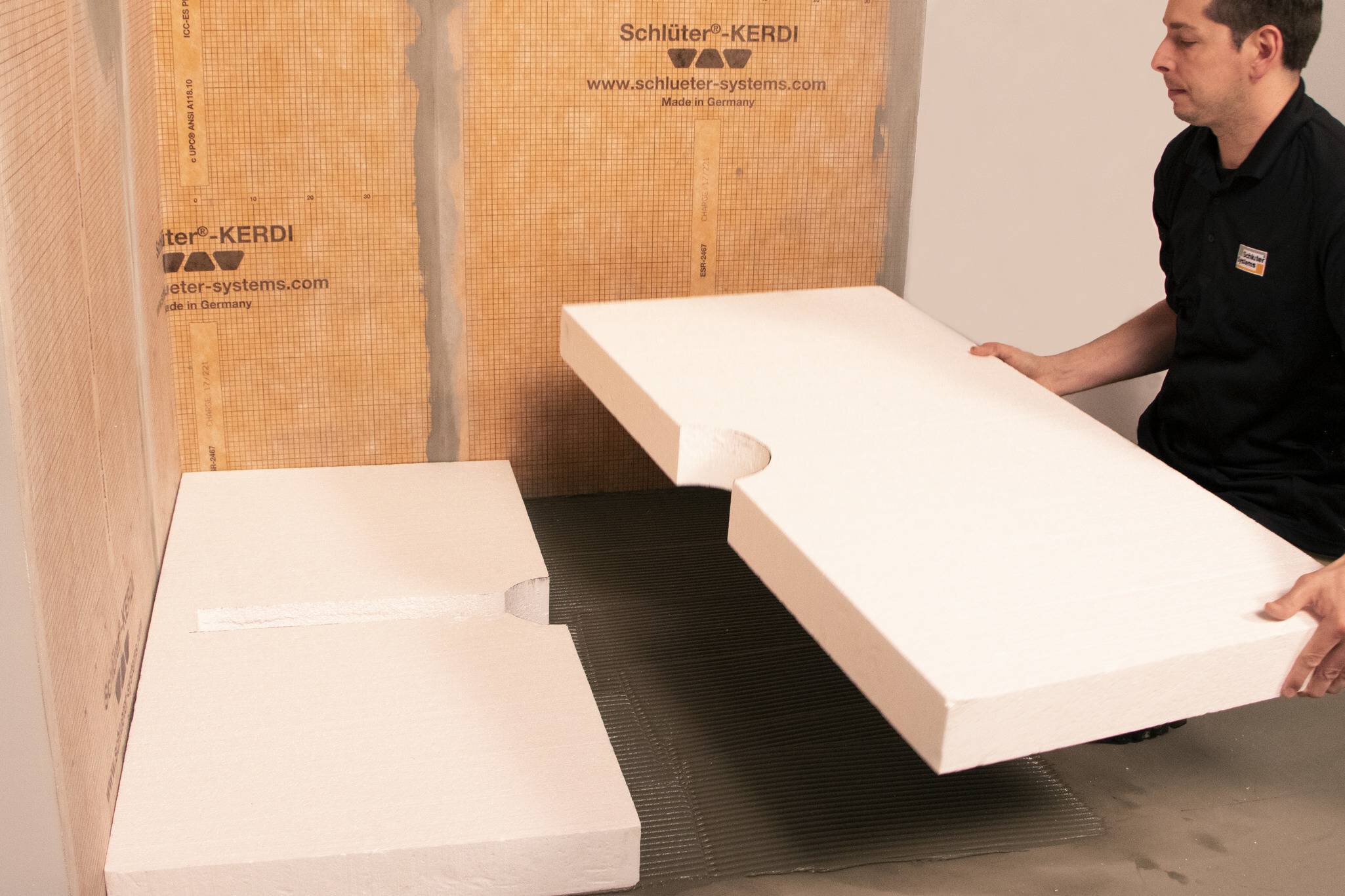 Un installateur encastre la plaque de compensation Schluter-KERDI-SHOWER-CB dans le substrat.