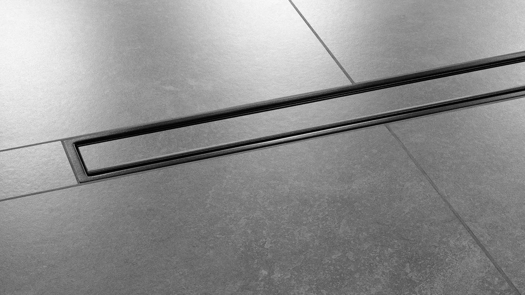 Gros plan sur un sol de douche avec carrelage de couleur gris fonc&eacute; et caniveau Schl&uuml;ter-KERDI-LINE-C install&eacute; au centre de la douche, design FRAMED TILE, finition TRENDLINE, noir graphite mat.