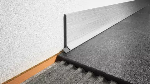 Nahaufnahme eines Boden-Wand-&Uuml;bergangs mit einem Schl&uuml;ter-DESIGNBASE-SL Sockelprofil in geb&uuml;rstetem Aluminium