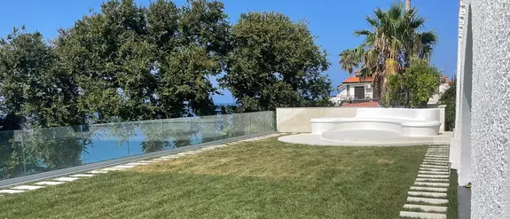 Una terrazza sul tetto con vista sul cielo azzurro e sulle palme, con prato e ringhiera in vetro